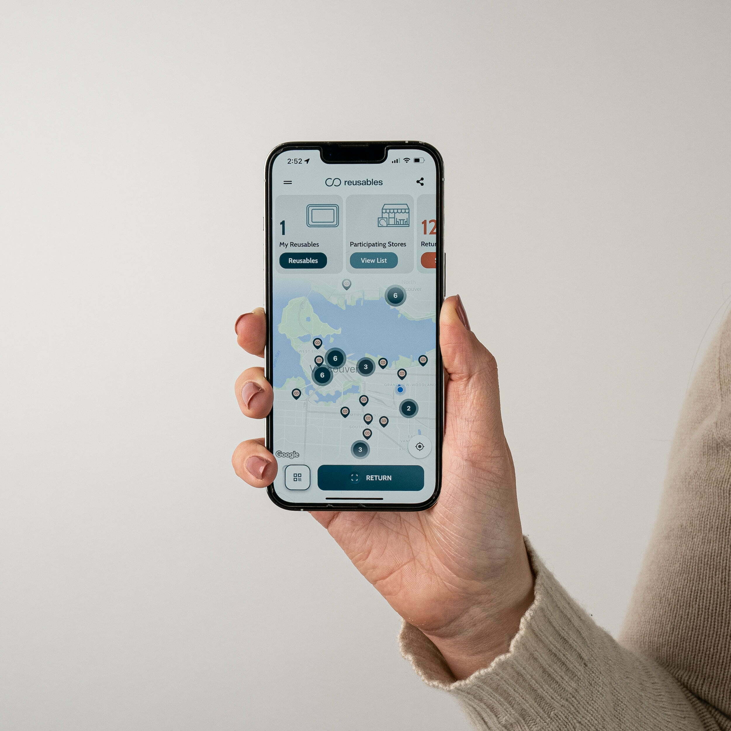 The creative shows a person's hand holding a mobile with the Reusables app open. The mobile screen shows the map of Vancouver highlighting Reusers and participating stores.